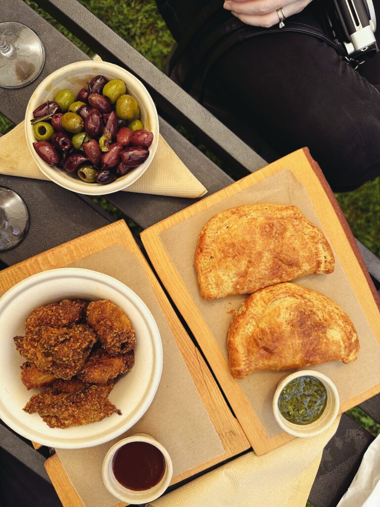 A small feast of snacks. Clockwise: a dish of olives, two empanadas with chimichurri, and a bowl of crispy tandoori chicken with a sauce.